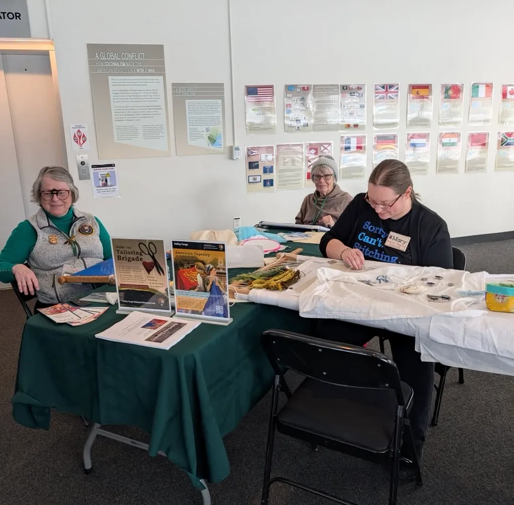Co-Director Mary Van Tyne stitches on the panel alongside volunteers